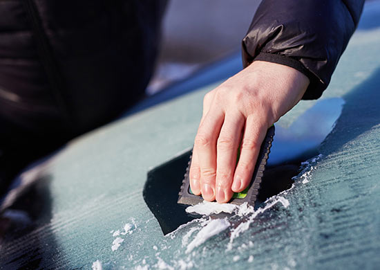 Limpiar la ventana trasera del coche de nieve con un raspador de