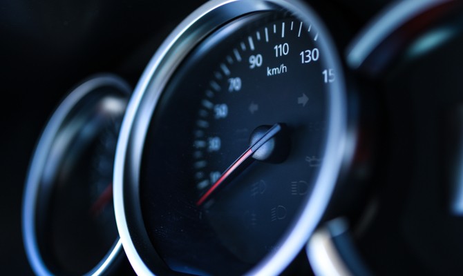 A speedometer in a car's dash, showing the red needle placed at zero miles per hour.