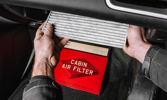 Mechanic replacing a cabin air filter with a new Champion cabin air filter.