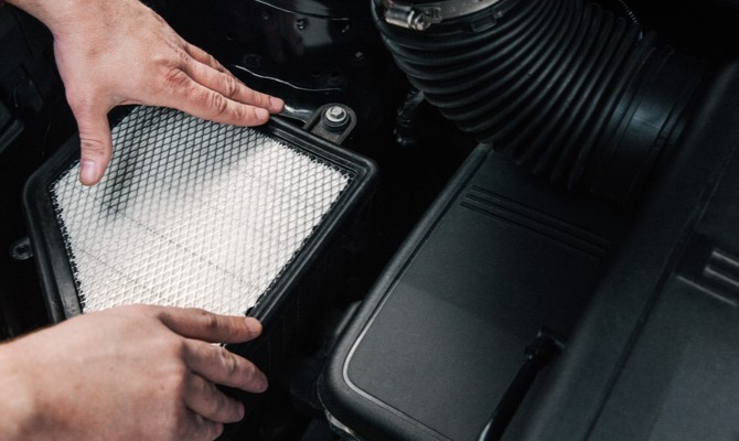 mechanic-installing-car-engine-air-filter A man replacing a dirty air filter on a vehicle.