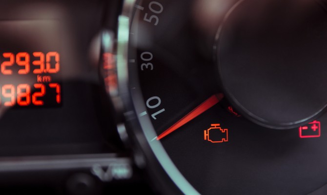 car-check-engine-light-battery-light-illuminated A speedometer in a car's dash showing the red needle placed at zero miles per hour, with a couple additional warning lights illuminated.