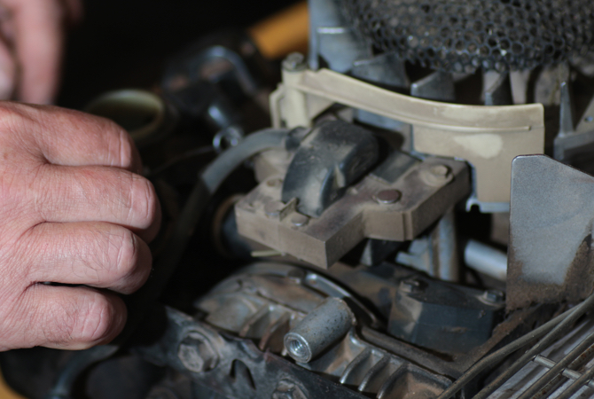 A close up of a hand working on a lawnmower engine