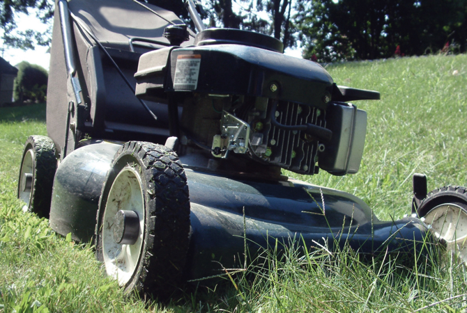 Close up of a lawn mover cutting grass in what looks to be someone's yard