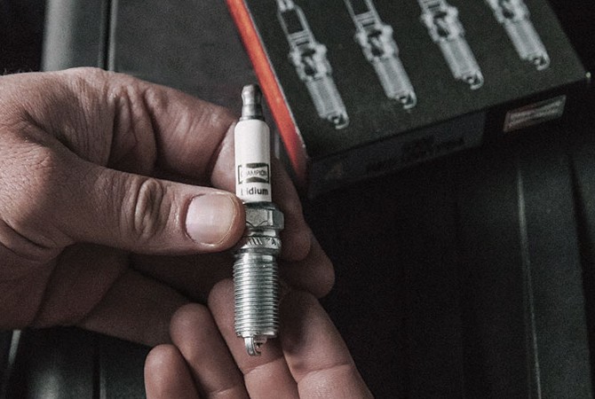 Hands holding a spark plug next to Champion box