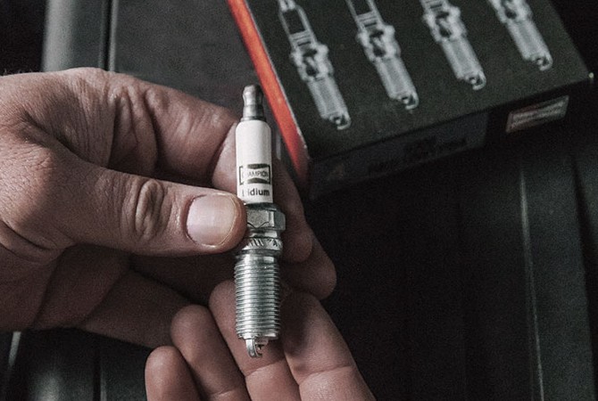 technician-holding-champion-iridium-spark-plug Hands holding a spark plug next to Champion box